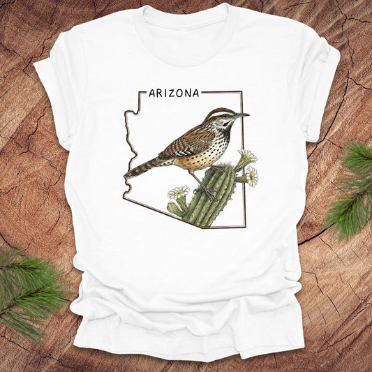 White t-shirt with Arizona state outline with cactus wren and cactus flower design on a wooden surface