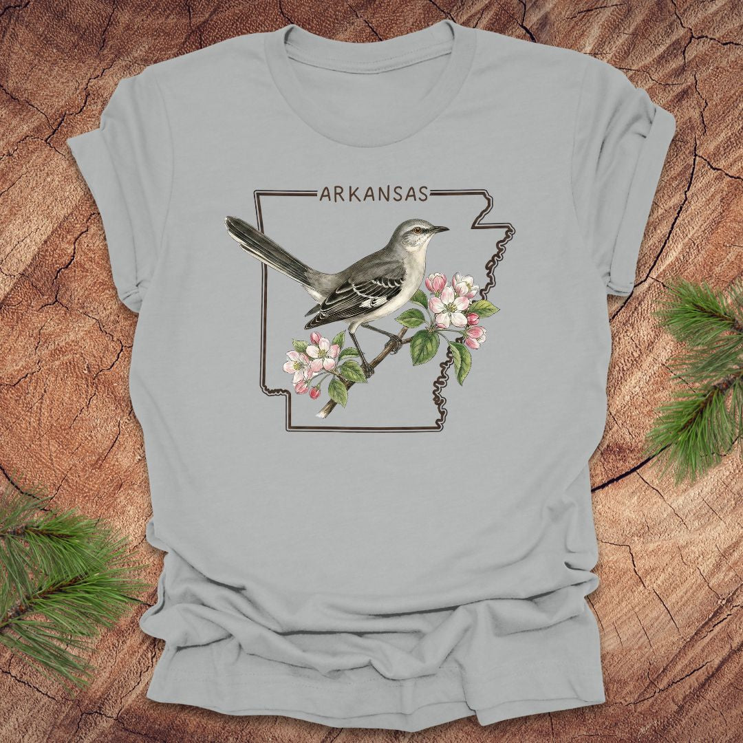 Gray t-shirt with Arkansas state outline and bird design on a wooden surface