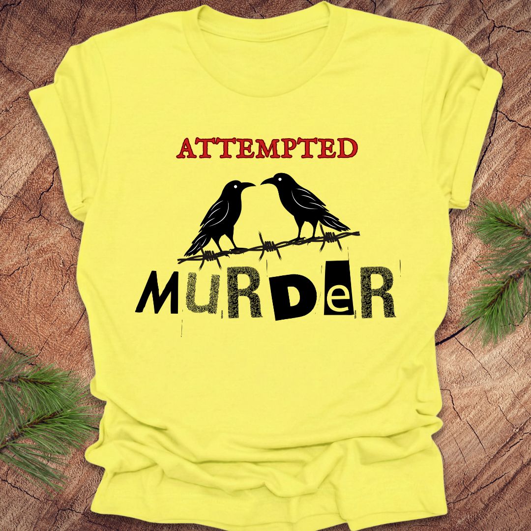 Yellow t-shirt with black and red text and crow design on a wooden surface.
