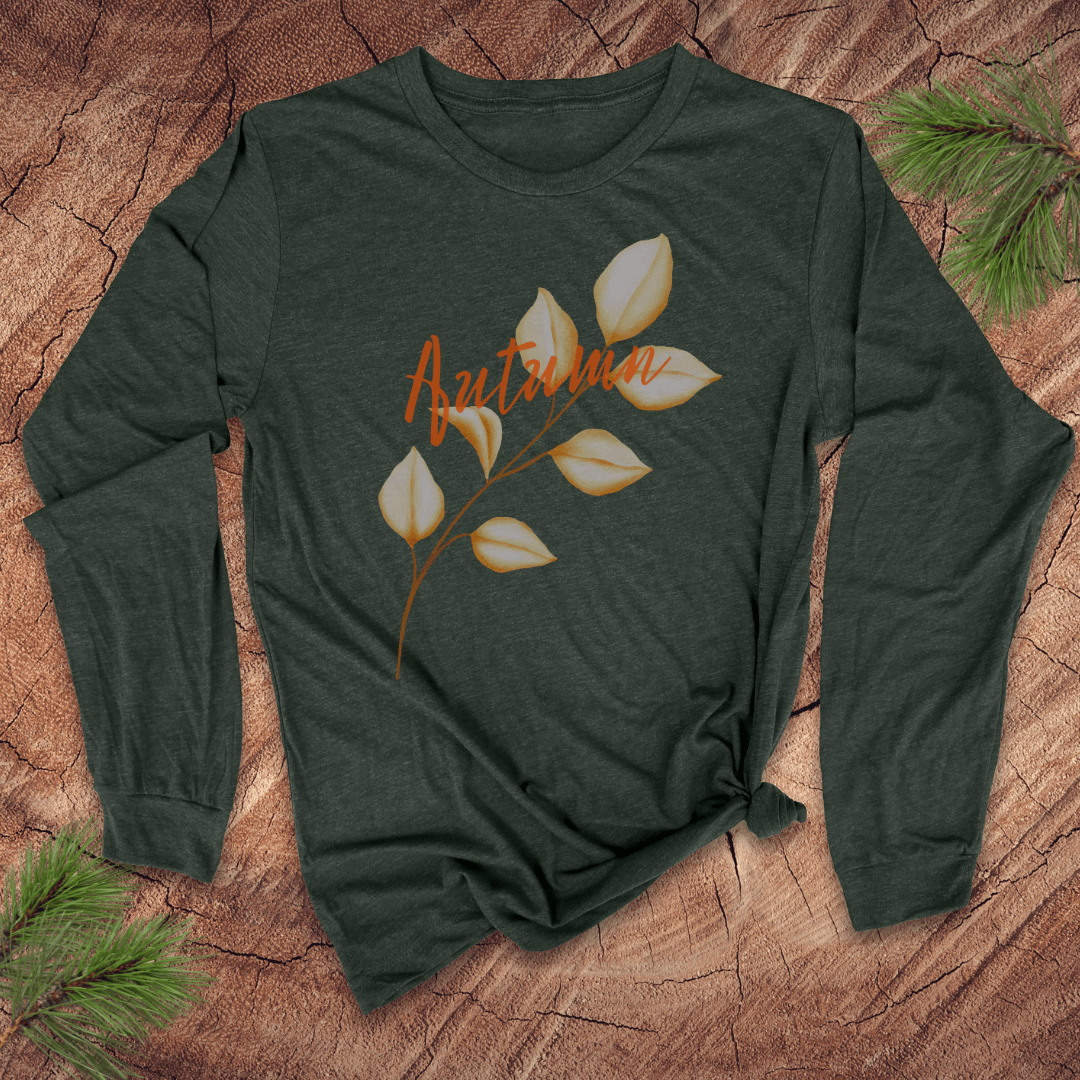 green long sleeve tshirt with the word autumn and a long stemmed leaf, on a wood background with pine leaves