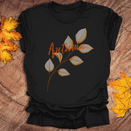 Black t-shirt with 'Autumn' and leaf design on a wooden surface with fall leaves.
