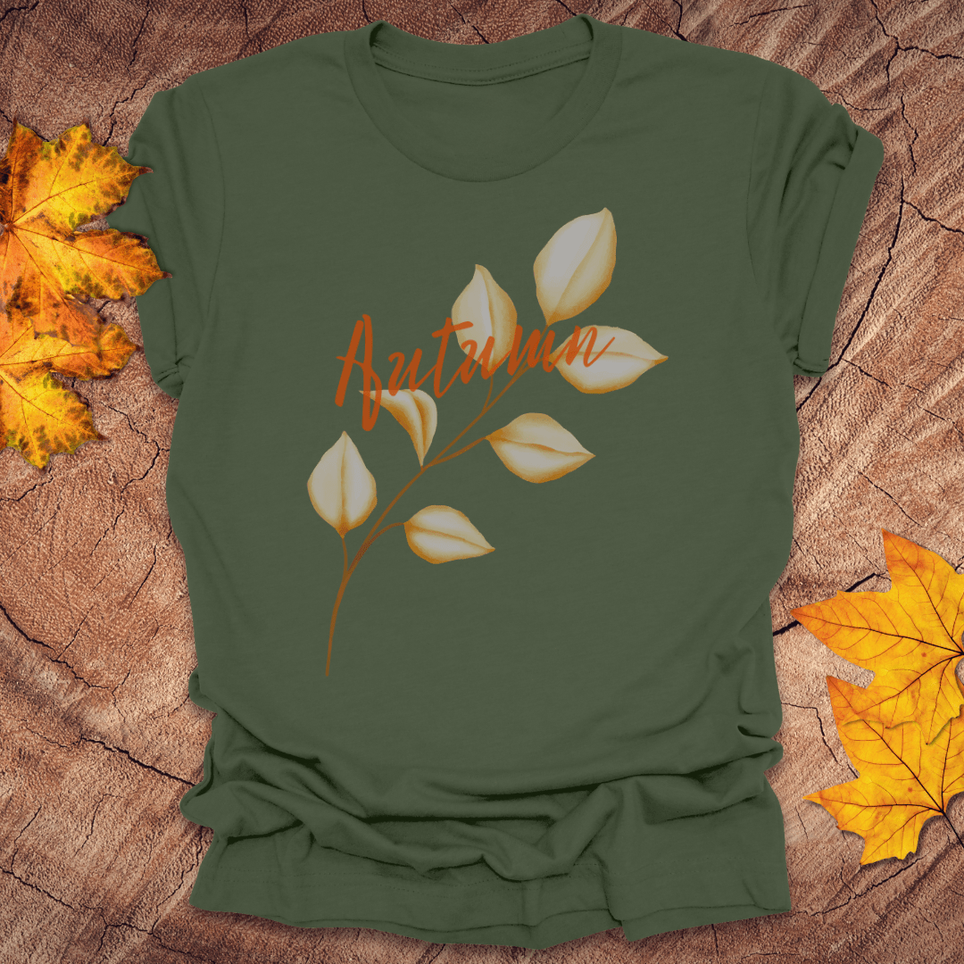 Green t-shirt with 'Autumn' design on a wooden surface with fall leaves.