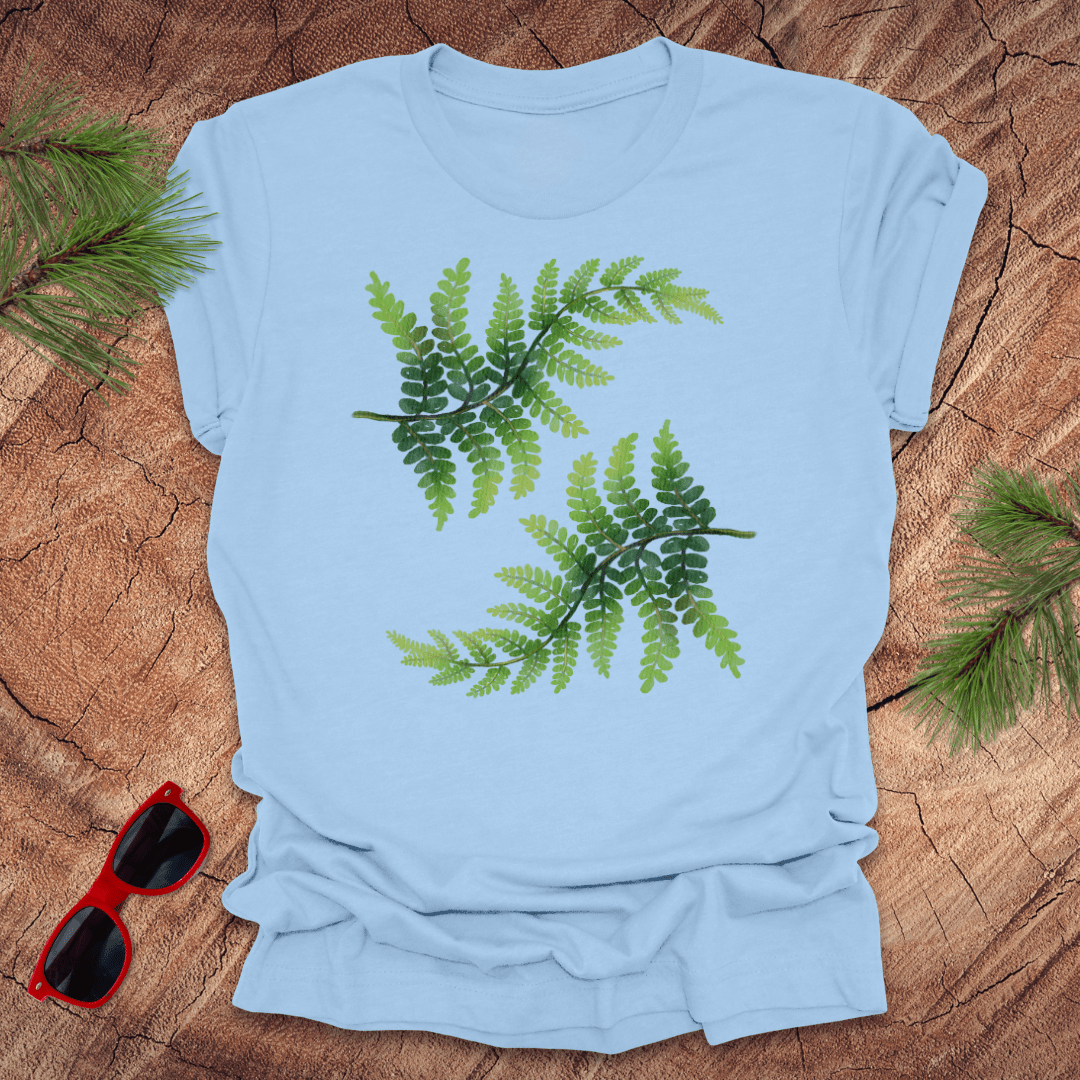 Light blue t-shirt with green leaf design on a wooden surface with sunglasses and leaves.