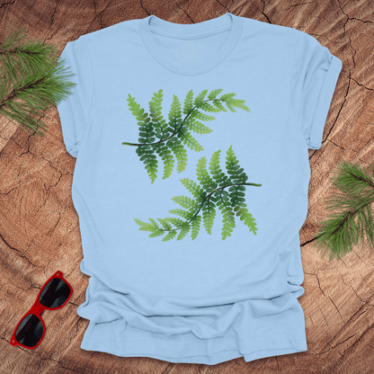 Light blue t-shirt with green leaf design on a wooden surface with sunglasses and leaves.