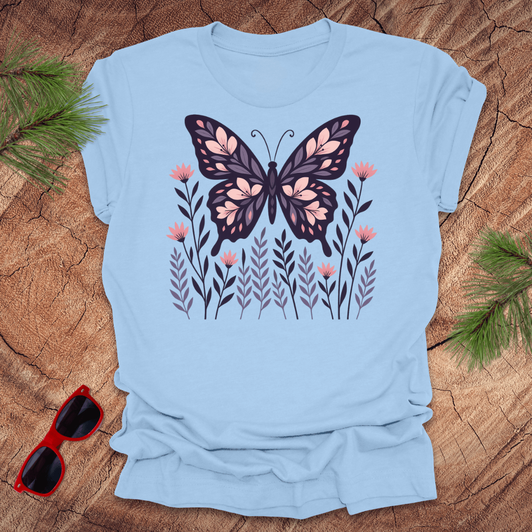 Baby blue t-shirt with a butterfly and flower design on a wooden surface with sunglasses and leaves.