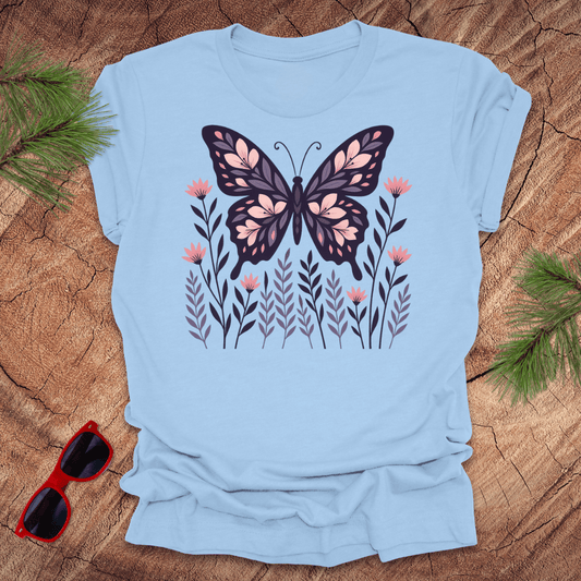 Baby blue t-shirt with a butterfly and flower design on a wooden surface with sunglasses and leaves.