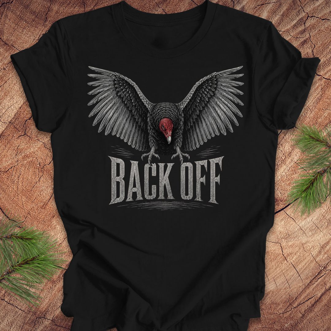A black short-sleeve t-shirt laid flat on a rustic wood surface, featuring a large graphic of a spreading-wing vulture with a red head and the text 'BACK OFF' in distressed white lettering.