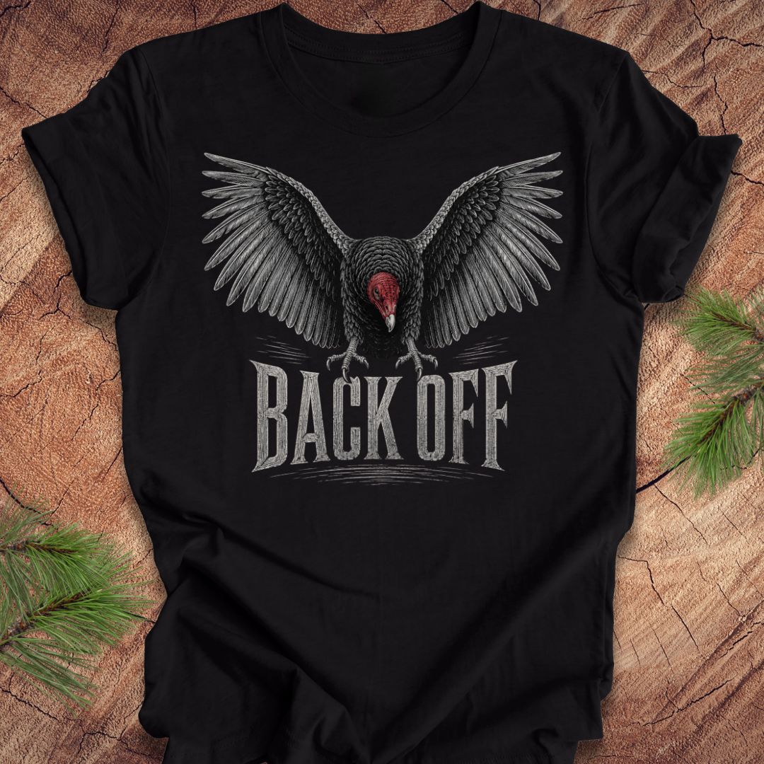 A black short-sleeve t-shirt with a graphic of a vulture with wings spread and the text 'BACK OFF' underneath, displayed on a rustic wood background with pine branches.
