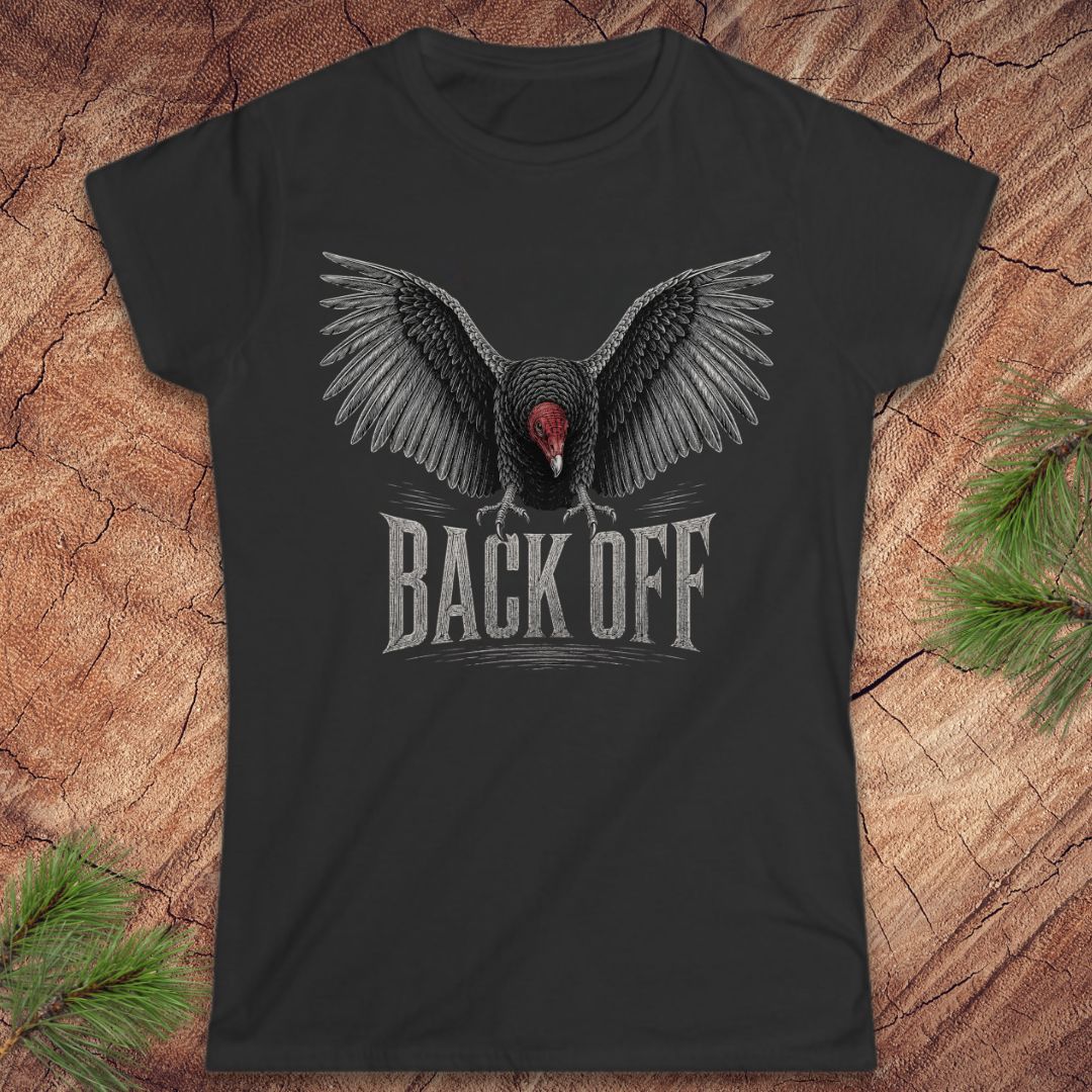 A black short-sleeve t-shirt with a graphic of a vulture with outstretched wings and the text 'BACK OFF' underneath, displayed flat on a rustic wood background with pine branches in the corners.