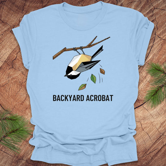 Light blue t-shirt with a chickadee graphic and 'Backyard Acrobat' text on a wooden surface.