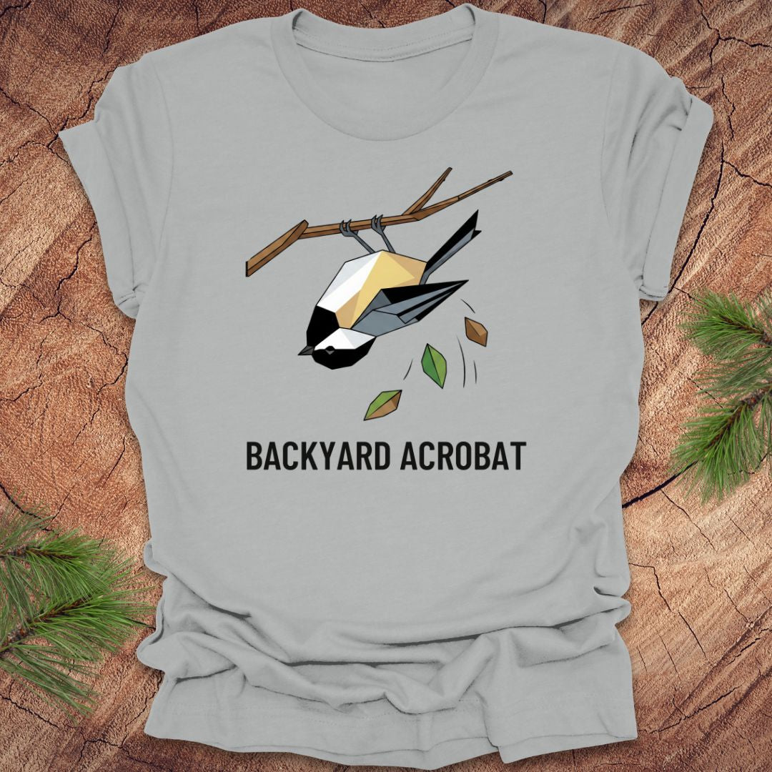 Silver t-shirt with a chickadee graphic and 'Backyard Acrobat' text on a wooden surface.
