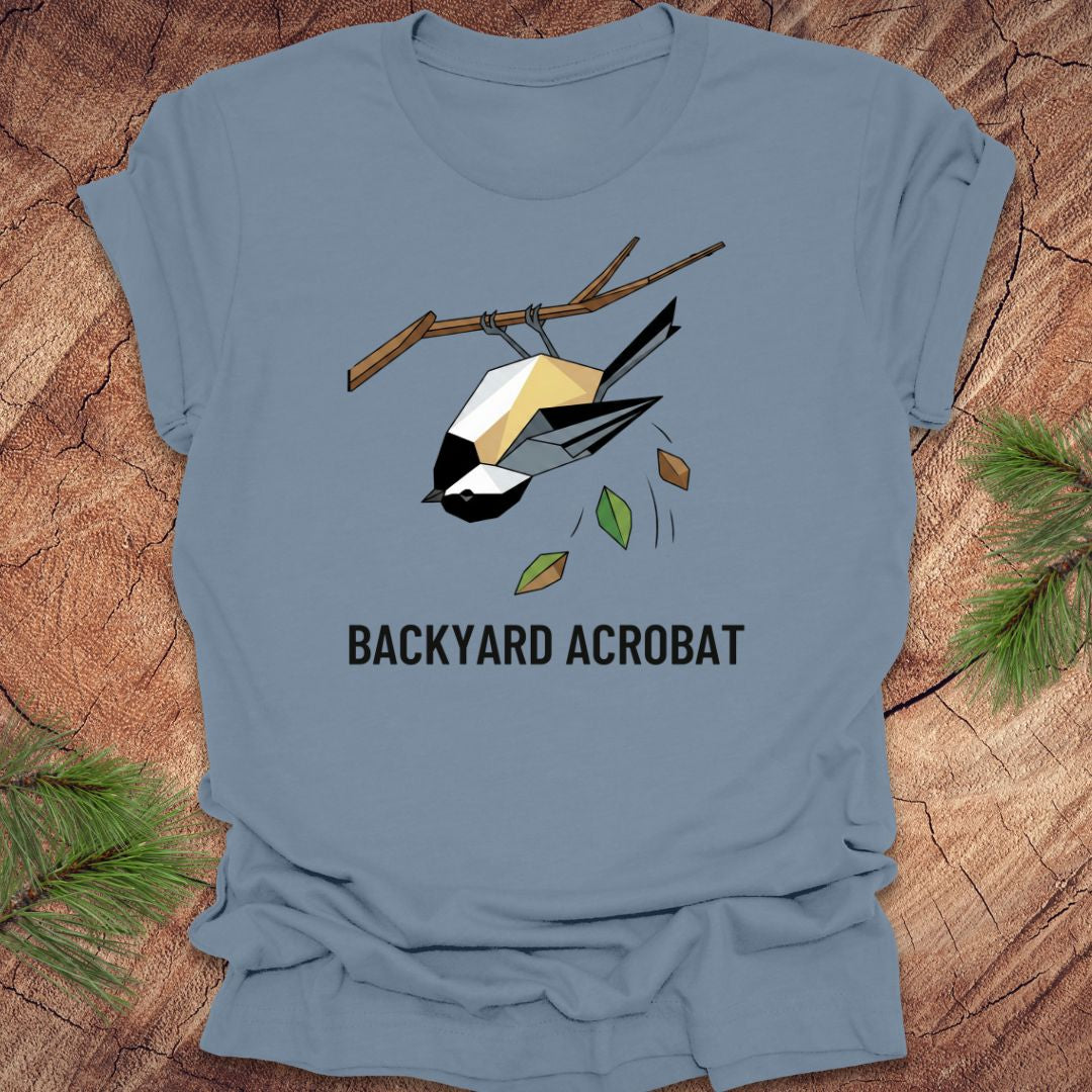 Steel blue t-shirt with a chickadee graphic and 'Backyard Acrobat' text on a wooden surface.