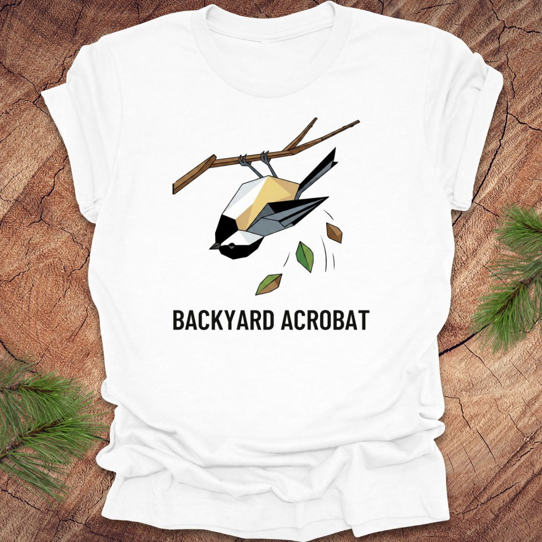 White t-shirt with a chickadee graphic and 'Backyard Acrobat' text on a wooden surface.