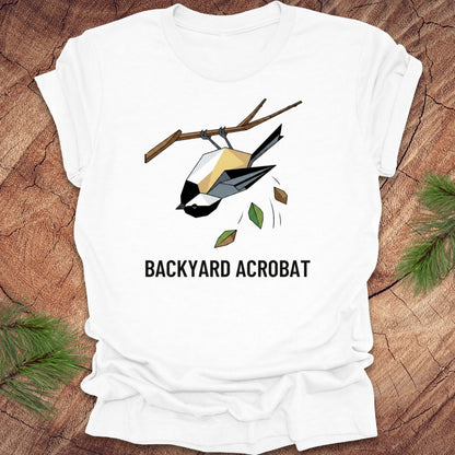 White t-shirt with a chickadee graphic and 'Backyard Acrobat' text on a wooden surface.