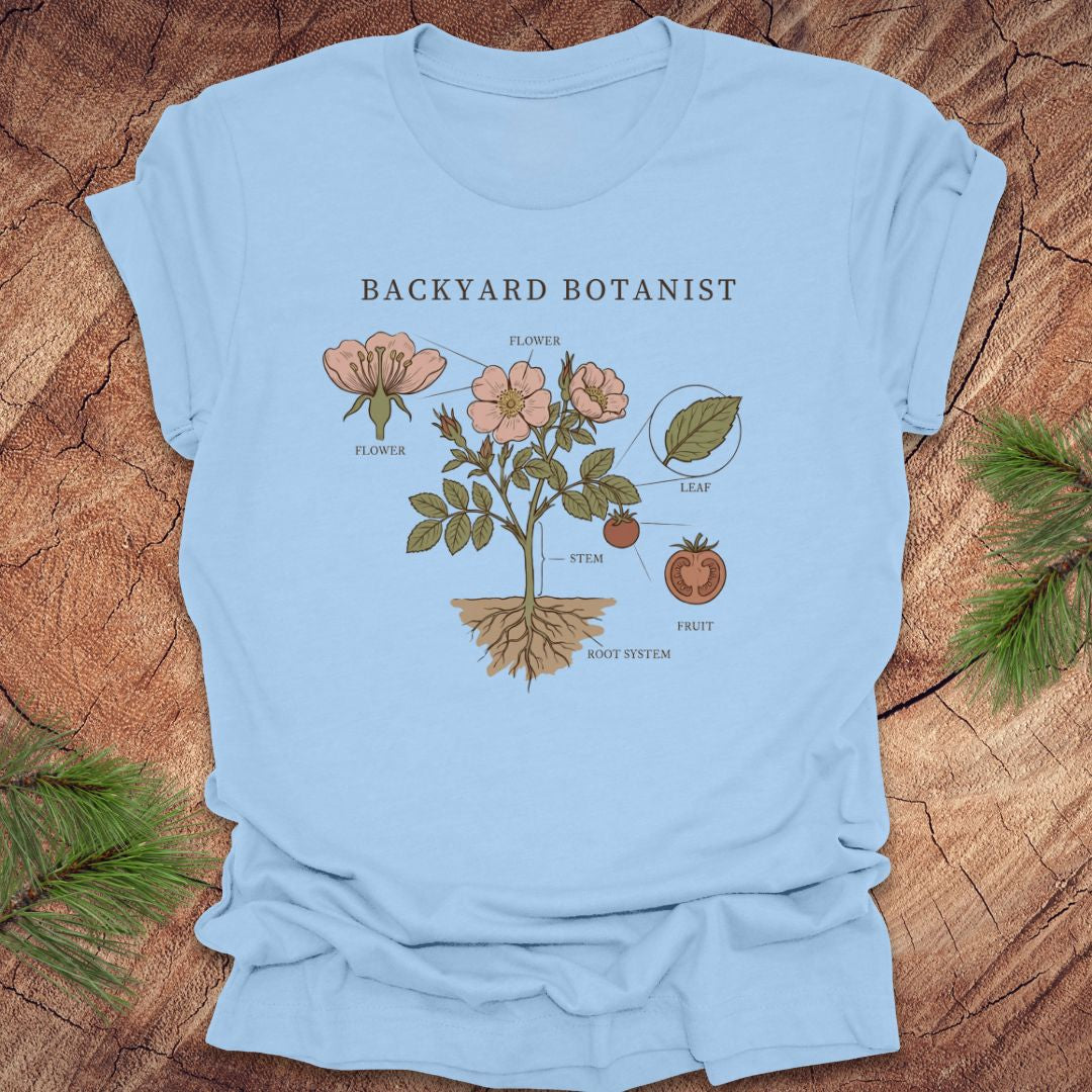 Light blue t-shirt with botanical design and 'Backyard Botanist' text on a wooden surface.