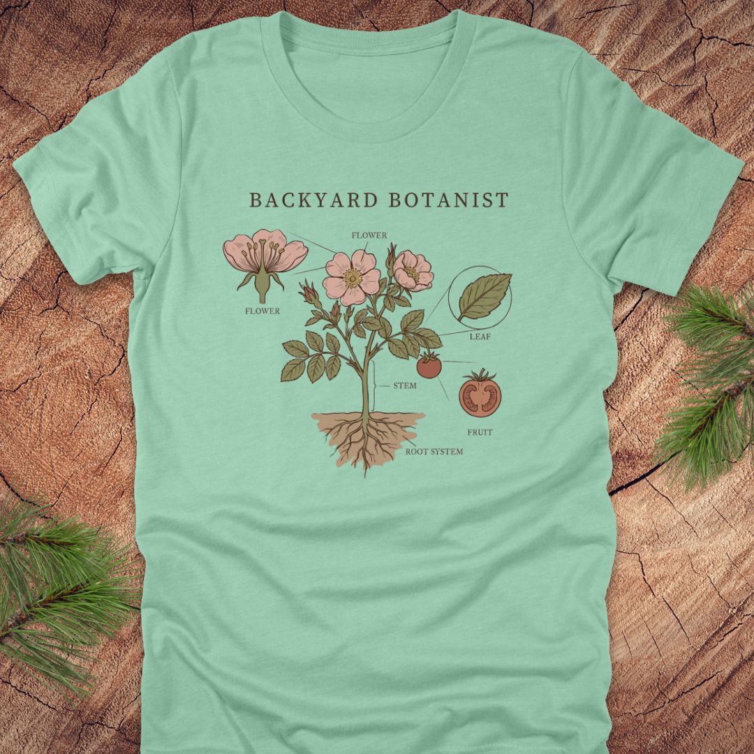 Light green t-shirt with botanical design and 'Backyard Botanist' text on a wooden surface.