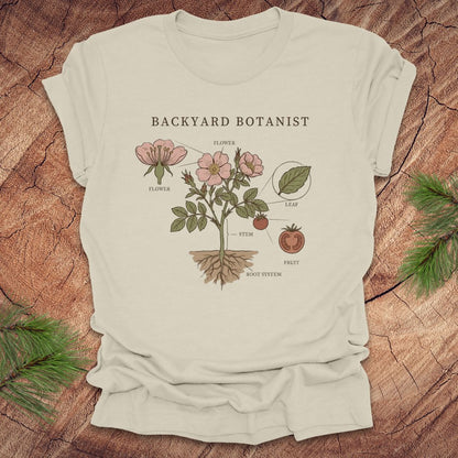 Beige t-shirt with botanical design and 'Backyard Botanist' text on a wooden surface.