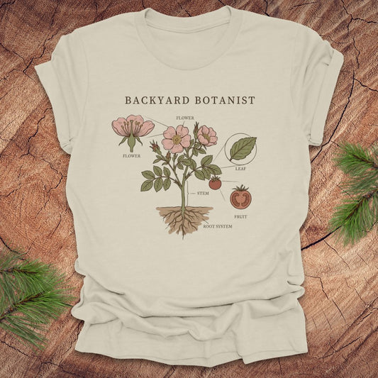Beige t-shirt with botanical design and 'Backyard Botanist' text on a wooden surface.