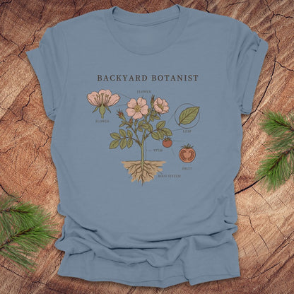 Blue t-shirt with botanical design and 'Backyard Botanist' text on a wooden surface.