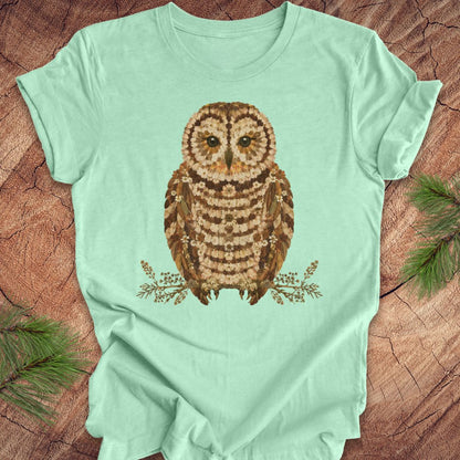 Mint green t-shirt with an owl and flower design on a wooden surface
