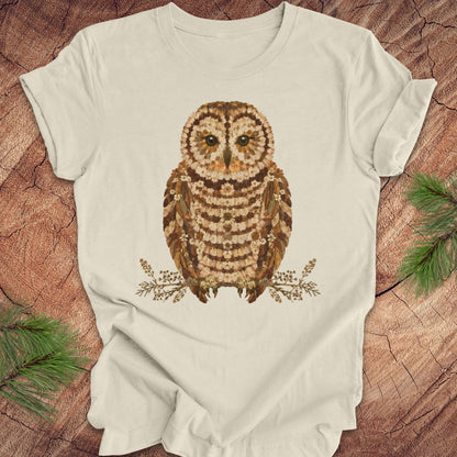 Beige t-shirt with an owl and flower design on a wooden surface