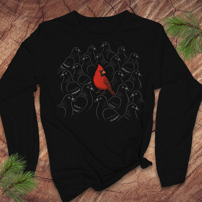 Black long-sleeve t-shirt with a bright red Cardinal standing out in a crowd of gray line-drawn pigeons, laid flat on a rustic wood background with pine branches.