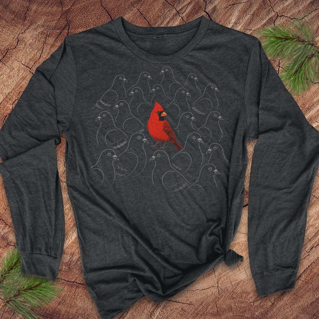Dark grey heather long-sleeve t-shirt with a bright red Cardinal standing out in a crowd of gray line-drawn pigeons, laid flat on a rustic wood background with pine branches.