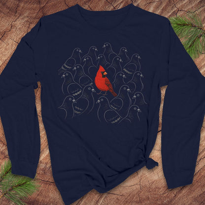 Navy long-sleeve t-shirt with a bright red Cardinal standing out in a crowd of gray line-drawn pigeons, laid flat on a rustic wood background with pine branches.