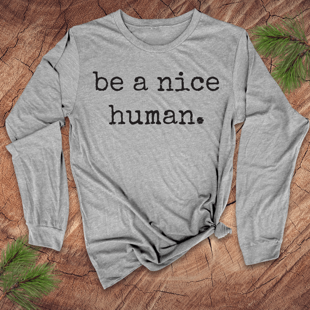 Gray long sleeve shirt with 'be a nice human' text on a wooden surface with greenery.