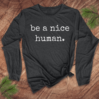 Dark gray long sleeve shirt with 'be a nice human' text on a wooden surface with greenery.