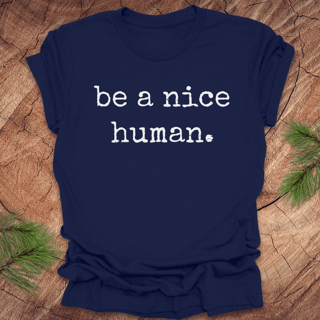 Navy blue t-shirt with 'be a nice human' text on a wooden surface with greenery.
