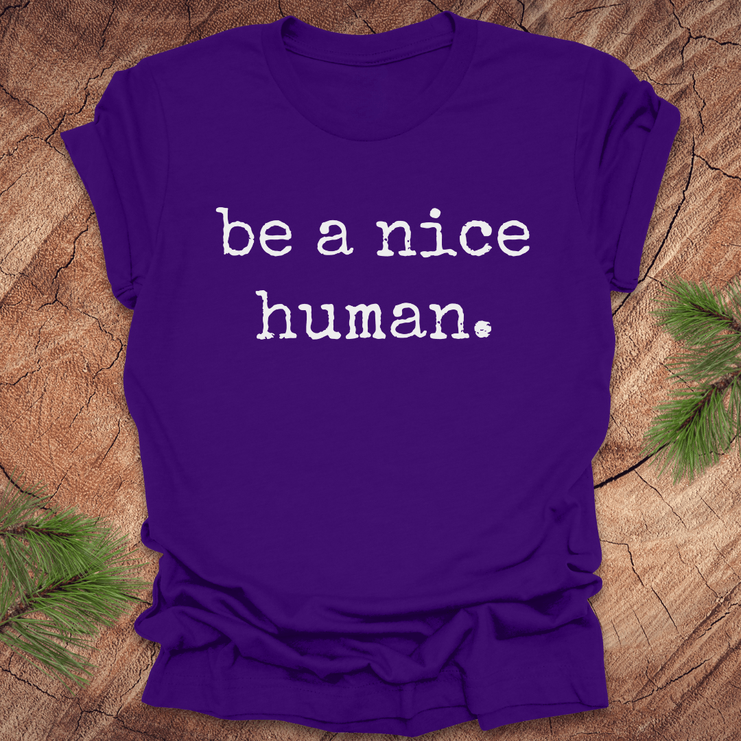 Purple t-shirt with 'be a nice human' text on a wooden surface