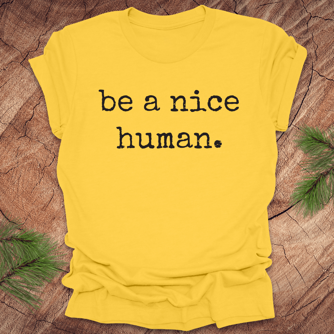 Yellow t-shirt with 'be a nice human' text on a wooden surface