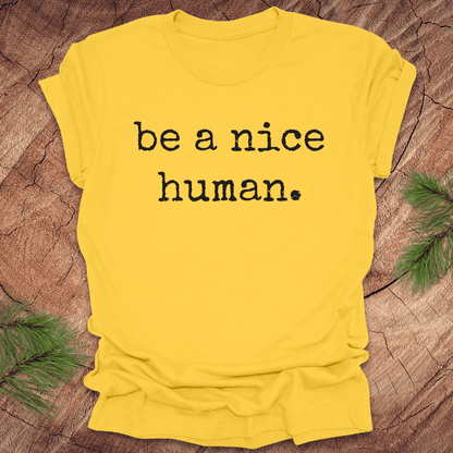 Yellow t-shirt with 'be a nice human' text on a wooden surface