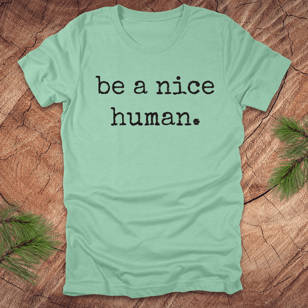 Mint green t-shirt with 'be a nice human' text on a wooden surface