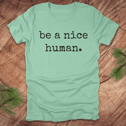 Mint green t-shirt with 'be a nice human' text on a wooden surface