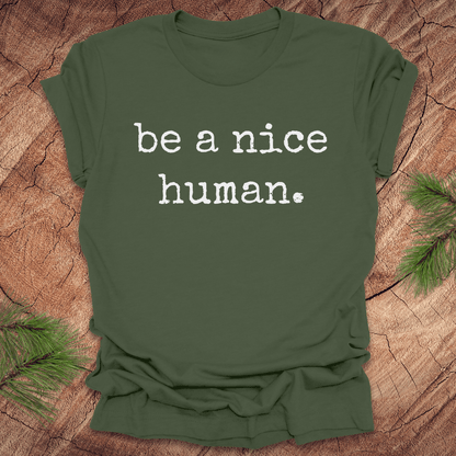 Green t-shirt with 'be a nice human' text on a wooden surface