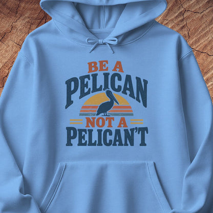 Carolina blue hoodie with a Brown Pelican silhouette on a retro striped sunset and the words BE A PELICAN NOT A PELICAN'T, laid flat on a rustic wood background.