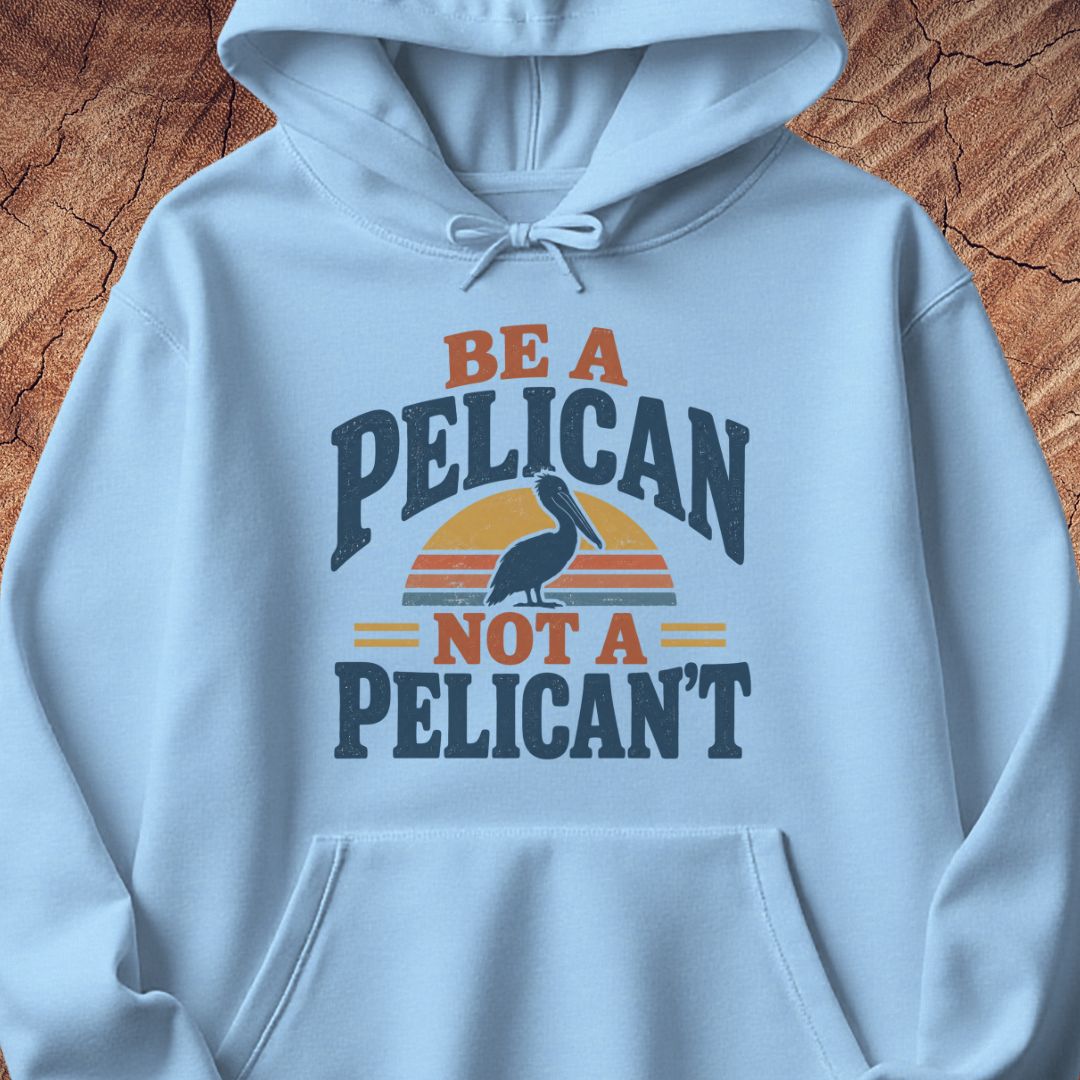 Light blue hoodie with a Brown Pelican silhouette on a retro striped sunset and the words BE A PELICAN NOT A PELICAN'T, laid flat on a rustic wood background.