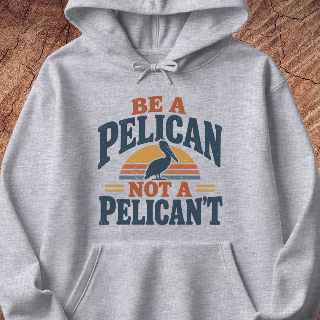 Sport grey hoodie with a Brown Pelican silhouette on a retro striped sunset and the words BE A PELICAN NOT A PELICAN'T, laid flat on a rustic wood background.