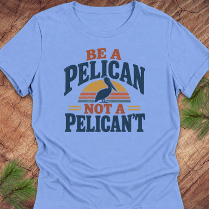 Carolina blue women's relaxed t-shirt with a Brown Pelican silhouette on a retro striped sunset and the words BE A PELICAN NOT A PELICAN'T, laid flat on a rustic wood background with pine branches.