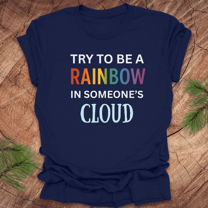 Navy blue t-shirt with colorful text 'Try to be a rainbow in someone's cloud' on a wooden surface