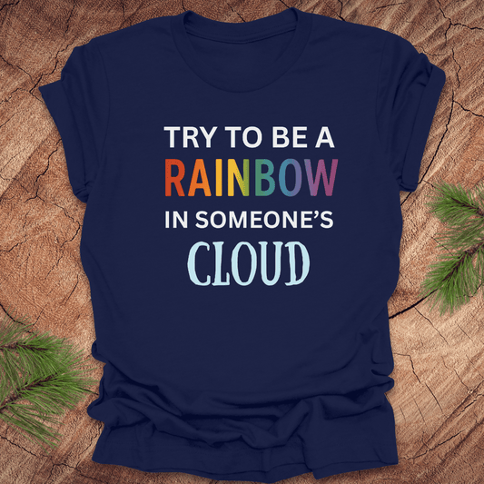 Navy blue t-shirt with colorful text 'Try to be a rainbow in someone's cloud' on a wooden surface