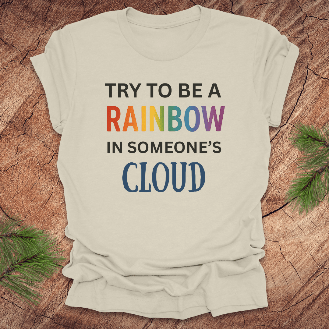 Beige t-shirt with colorful text 'Try to be a rainbow in someone's cloud' on a wooden surface
