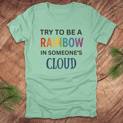 Mint green t-shirt with colorful text 'Try to be a rainbow in someone's cloud' on a wooden surface