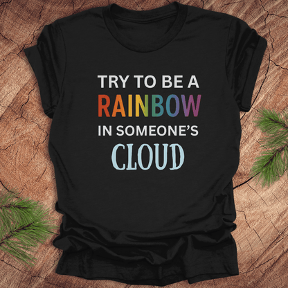Black t-shirt with colorful text 'Try to be a rainbow in someone's cloud' on a wooden surface