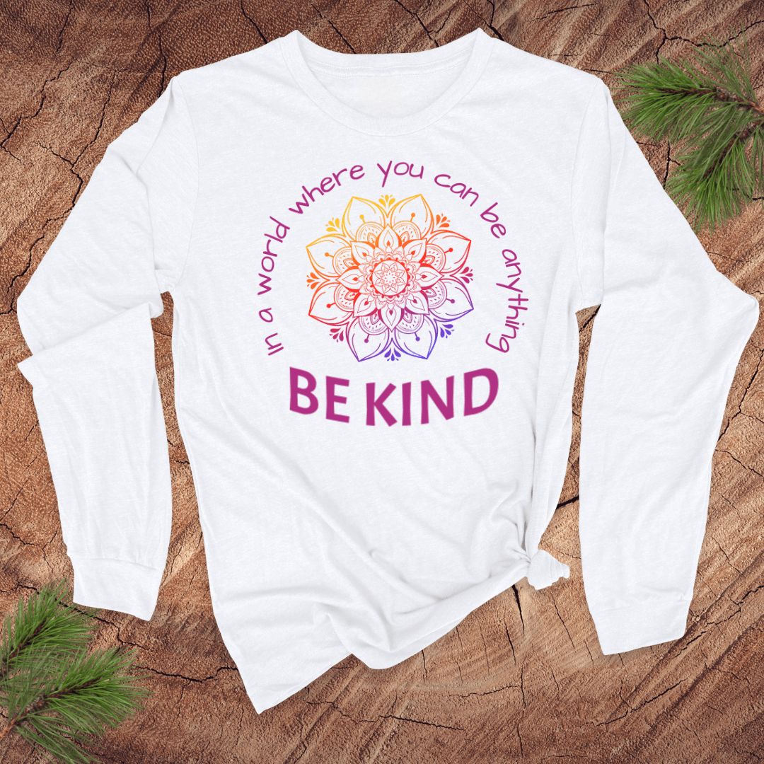 White long-sleeve shirt with a colorful mandala and 'Be Kind' text on a wooden surface.