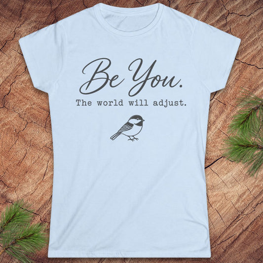 A light blue short-sleeve t-shirt with a black graphic print that reads 'Be You. The world will adjust.