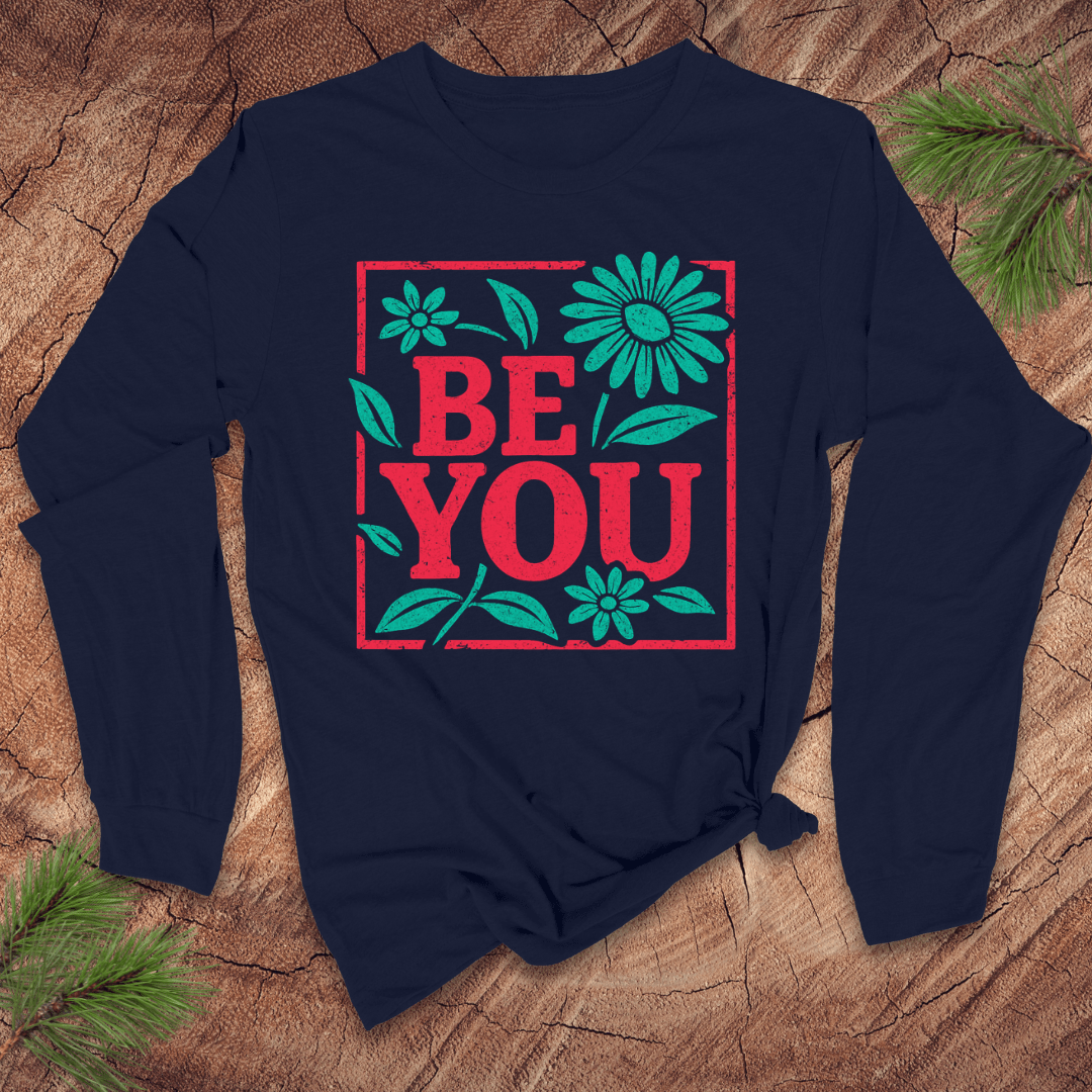 Navy blue long-sleeve shirt with 'BE YOU' text and floral design on a wooden surface.