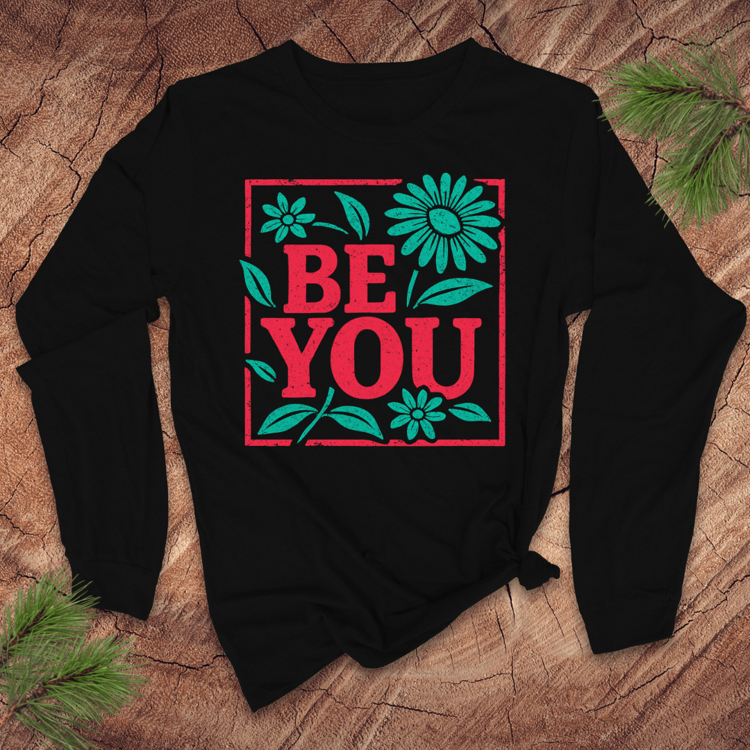 Black long-sleeve tshirt with 'BE YOU' text and floral design on a wooden surface